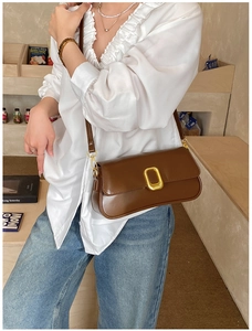 Detail of dark brown leather crossbody bag with a large golden buckle worn by a model