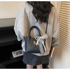 Detail of black lychee leather bucket bag with lace pearl bow charm on a model's back