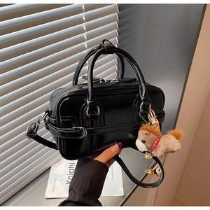 Detail of glossy black leather handbag with decorative straps and a cute horse charm