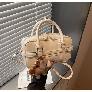 Detail of cream leather bowling bag with side buckle and plush horse charm accessory