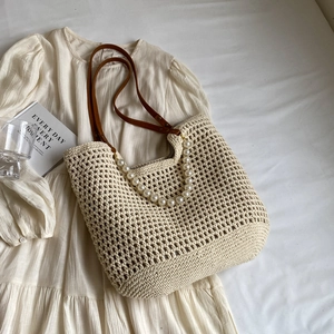 Close-up of handmade straw tote bag featuring round pearl handle and leather shoulder strap