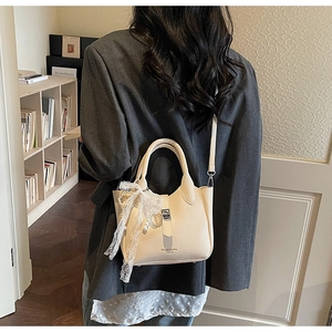 Detail showing creamy white bucket bag with lace bow and pearl charm on a model