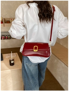 Detail of red leather square bag featuring a gold metal buckle in a cozy cafe setting