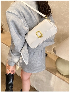 Close-up of minimalist cream leather shoulder bag with elegant gold buckle on model