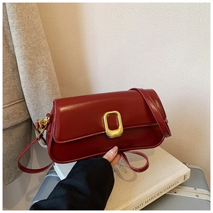 Detail of a deep red rectangular shoulder bag with golden metallic buckle on a white book