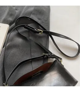 Detail of adjustable black leather shoulder strap with golden metal buckle on square bag