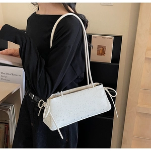 Detail of white baguette bag with star print and side drawstring bows on a model