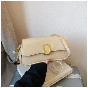 Close-up of cream leather shoulder bag with elegant gold metal buckle on top of books