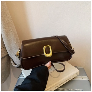 Detailed close-up of dark brown leather handbag with gold oval clasp on art books
