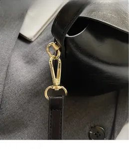 Close-up of golden metal clasp and black leather shoulder strap on a sleek handbag