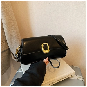 Detail of a black leather crossbody bag with a gold rectangular buckle on a casual setting