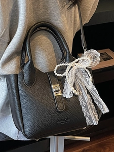 Chic black bucket bag with pearl lace bow charm and metallic clasp, worn crossbody style