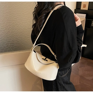 Detail of a creamy white glossy leather crossbody bag with a golden turn-lock clasp