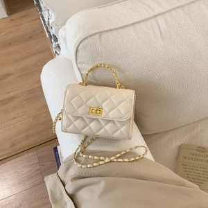 Detail einer gesteppten beigen Umhängetasche mit goldener Hardware auf einem Sofa