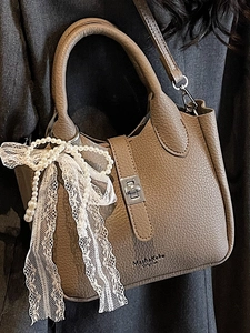 Brown litchi leather bucket bag with metal lock and pearl bow charm shown on model