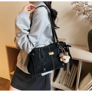 Detail of black tote bag featuring white contrast stitching and a cute teddy bear charm