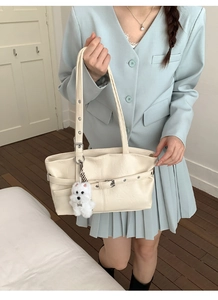 Détail du sac cabas en similicuir crème avec sangles à œillets et breloque chiot en peluche