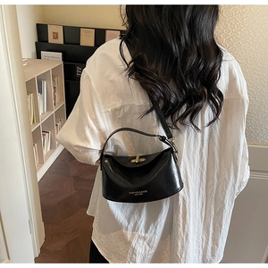 Rear view of a black crescent crossbody bag with gold buckle on a white shirt model