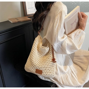 Detail view of woven shoulder bag with brown leather straps worn by model in home setting