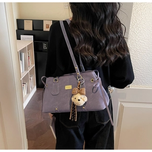 Detailed side view of purple leather tote bag with gold hardware and plush bear charm