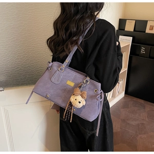 Detail view of purple suede tote bag with drawstring, gold hardware and teddy bear charm