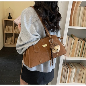 Detail view of retro brown tote bag featuring matte leather texture and teddy bear charm