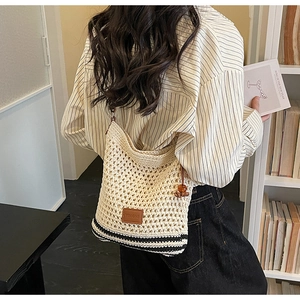 Detail of hand-woven beige crochet tote bag with striped bottom on model's shoulder