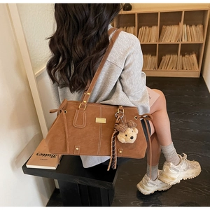 Brown suede tote bag with teddy bear pendant shown in a cozy library setting