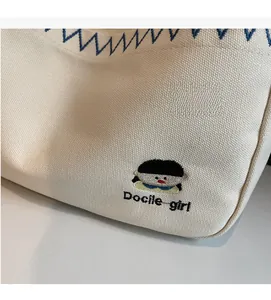 Detail of canvas shoulder bag with blue zigzag stitching and cartoon girl embroidery