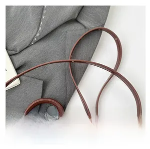 Detail of dark brown leather handbag featuring padded top handle and adjustable shoulder strap