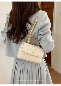 Detail einer cremefarbenen gesteppten kleinen Tasche mit goldener Kette am Modell