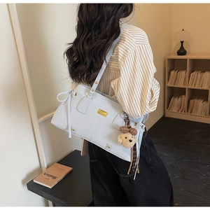 Detail of light blue leather tote bag with gold logo and cute bear pendant on a model