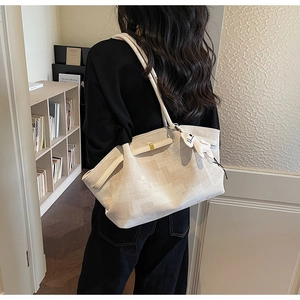 Detail of beige large tote bag with golden hardware and a white rabbit charm accessory
