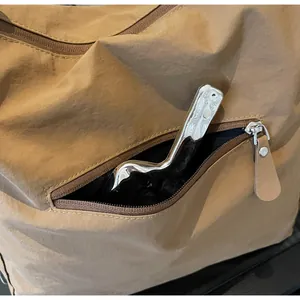 Detail view of khaki nylon shoulder bag featuring a front zipper pocket with leather puller