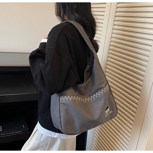 Close-up of charcoal canvas tote bag featuring white zigzag stitching and Docile-girl embroidery