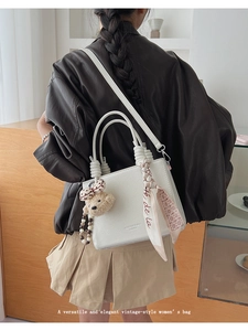 Detail of white lychee leather handbag with braided handles, plush bear charm and silk scarf