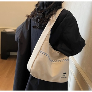 Detail view of beige canvas tote bag with blue zigzag stitching and Docile-girl logo