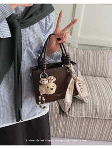 Detail of vintage brown patent leather handbag with a silk scarf and teddy bear charm