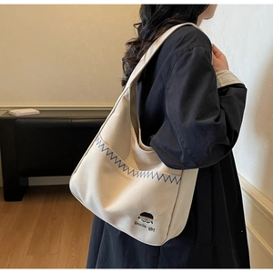 Close-up of cream canvas shoulder bag featuring blue zigzag stitching and girl embroidery