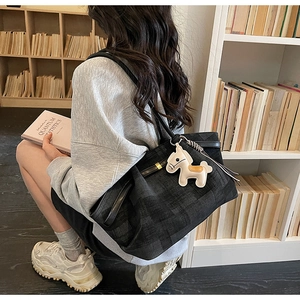 Detail of black textured tote bag with horse pendant and leather handles in a library setting