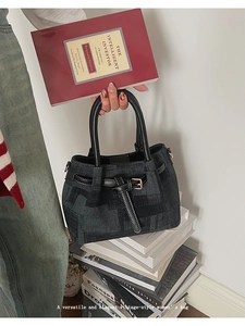 Detailed close-up of retro black denim handbag with leather buckle on stacked books