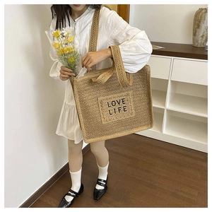 Gros plan du sac cabas tissé avec écusson LOVE LIFE et large bandoulière confortable
