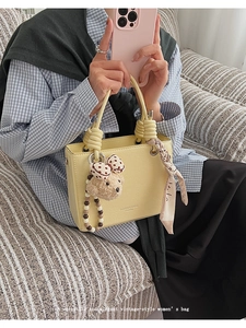 Detail view of yellow PU tote bag with knotted handle and plush bow charm decoration