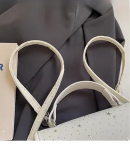 Close-up of white shoulder bag with silver star rivets on a business suit background