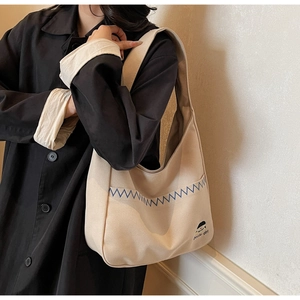 Detail of minimalist beige canvas hobo bag with blue zigzag embroidery and cartoon graphic