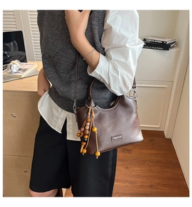 Close-up of a vintage brown bucket bag featuring wooden bead tassel and metal logo