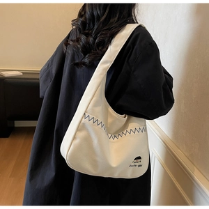 Detail of canvas hobo bag featuring blue zigzag stitching and Docile girl logo print