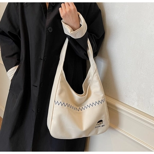 Detail shot of cream canvas tote bag with blue wave embroidery and cute cartoon print
