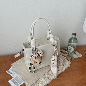 Detail of cream mini handbag with knotted handle, plush bear charm, and floral silk scarf