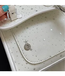Detail view of white canvas bag showing silver star patterns and metal magnetic buckle